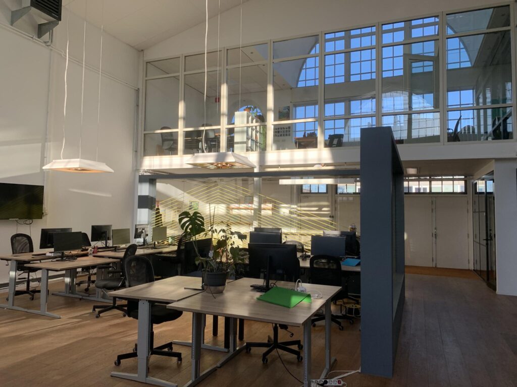 Moderne en lichte kantoorruimte aan het Gedempt Hamerkanaal met werkplekken, computers en grote ramen.